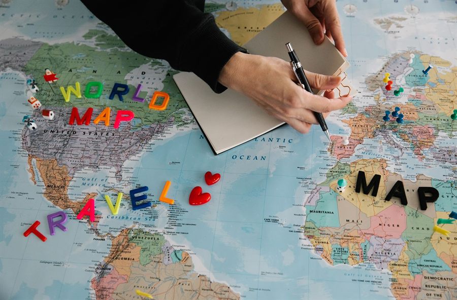 Hands planning a trip over a colorful world map with pins and a notebook, comparing river cruise deals