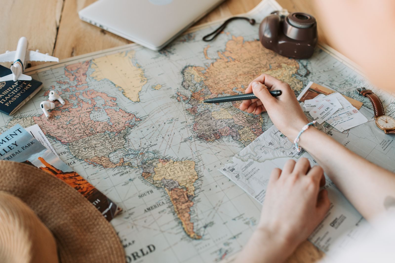 A traveler marking a route on a world map beside a passport and camera, the planning river cruise specialists do for you